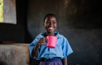 A girl smiles as she holds a pink mug of porridge
