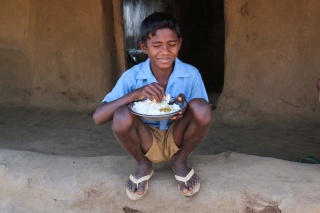 young boy sitting with a bowl of food in his hands