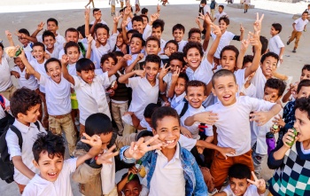 Image of a group of children holding up their hands and smiling into camera.