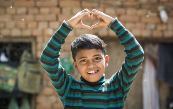A boy in India makes a heart gesture with his hands