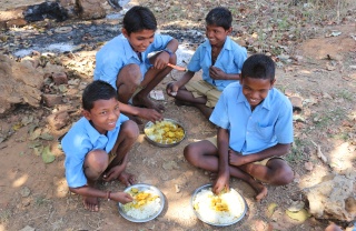 young boys kneeling on the ground eating from silver plates of food