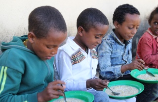 children sitting in a line eating from plates of food