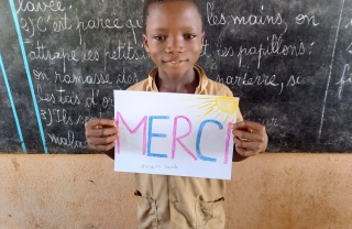 young child holding up a sign that reads "Merci"