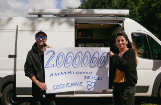 two fundraisers standing in front of a van and holding up a sign that reads "2000000"
