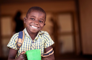 A boy in Zambia smiles while holding his green mug