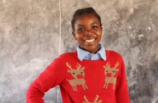 A child from Zambia smiling in school whilst wearing a red Christmas jumper.