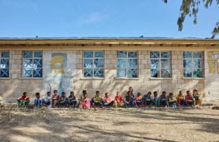 Children sitting outside of their school in a line enjoying their school meal.