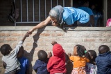 Mary's Meals staff member leaning out a window and touching hands with small children below