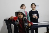 three children holding crafts in their hands and smiling