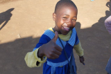 Child smiling and making a thumbs up gesture towards the camera.