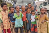 Group of children standing in front of parked vehicles.