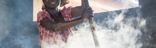 Woman stirring a large, steaming cauldron of hot food