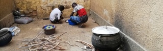 a stove sitting atop a bundle of wood with two people crouched in the corner of the room