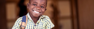 A boy in Zambia smiles while holding his green mug