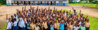 Children from Liberia waving outside of their primary school.