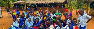 Children at school sitting outside with their cups for their daily school meal.