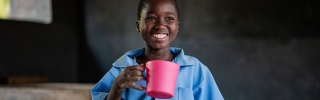 A girl smiles as she holds a pink mug of porridge