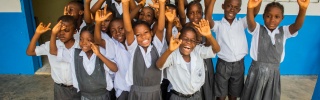 A class of children stand together cheering and waving in school