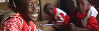 School children sitting at a desk in a red and white uniform.
