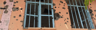 Image of school windows with bullet holes strewn across the outside wall.