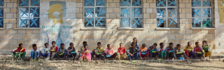 Image of children lined up eating food outside of school.