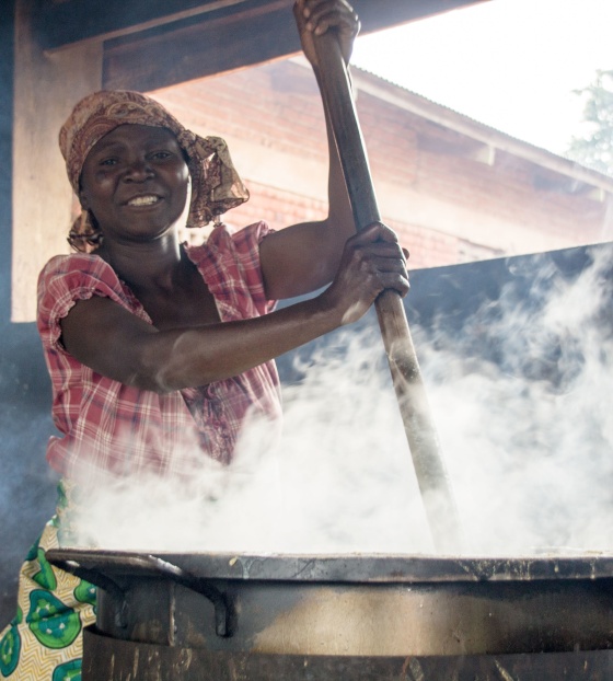 Woman stirring a large, steaming cauldron of hot food
