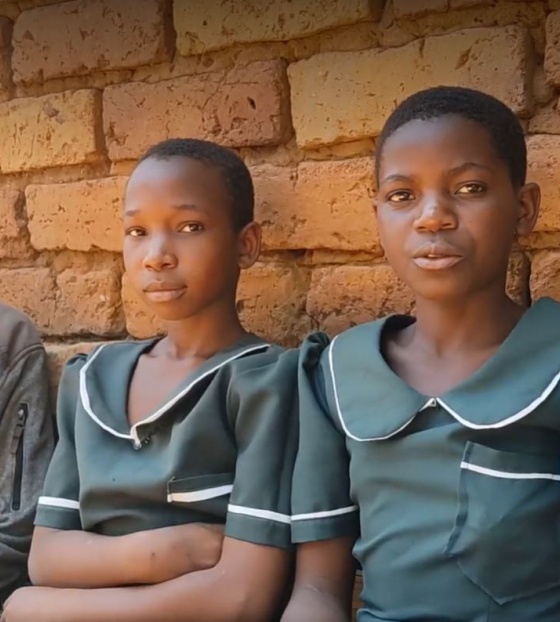 four women sitting against a wall, one is older than the other three