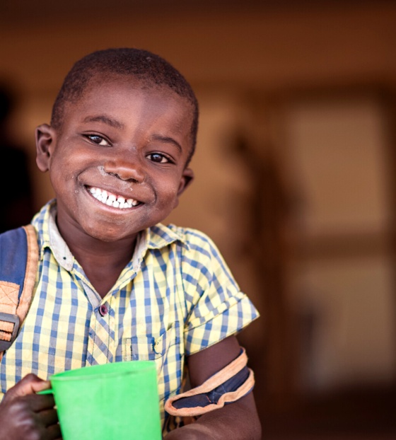 A boy in Zambia smiles while holding his green mug