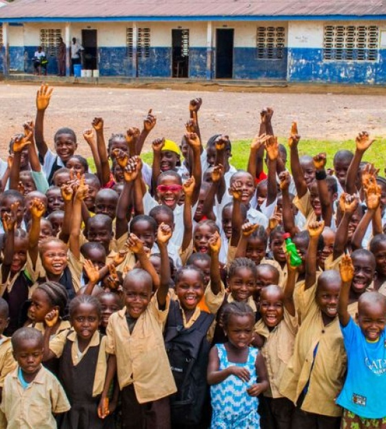 Children from Liberia waving outside of their primary school.