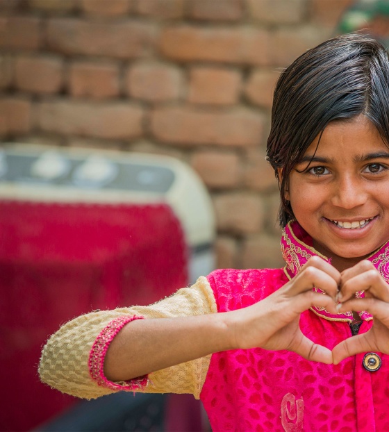 A girl in India makes a heart symbol with her hands