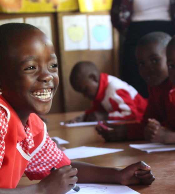 School children sitting at a desk in a red and white uniform.