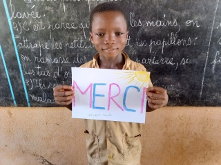 young child holding up a sign that reads "Merci"