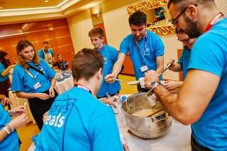 group of volunteers in blue t-shirts making a large pot of porridge together 
