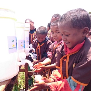 children in a line smiling as they wash their hands from a communal tap