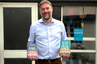Magnus MacFarlane-Barrow, founder of Mary's Meals smiling as he holds both books he has written. 