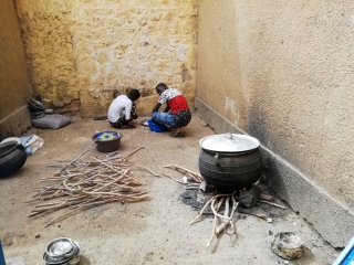 a stove sitting atop a bundle of wood with two people crouched in the corner of the room