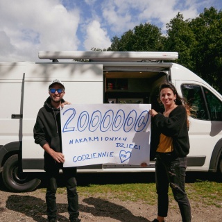 two fundraisers standing in front of a van and holding up a sign that reads "2000000"