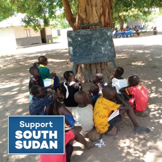 children in an outdoor school class gathered round a chalkboard on a tree