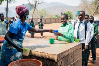 a queue of people collecting food from a woman serving behind a table