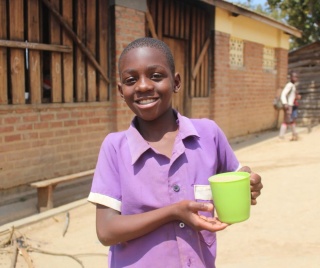 Shark, a school pupil from Malawi smiles and he holds his nutritious mug of porridge. 