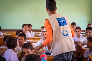 Mary's Meals volunteer speaking to children in a classroom. 