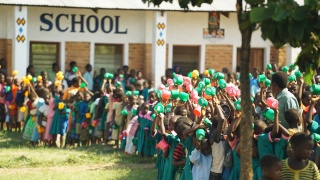 Children gathered outside of school in Malawi with their cups raised.