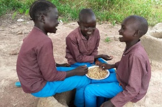 Three boys sitting together eating a meal and laughing. 