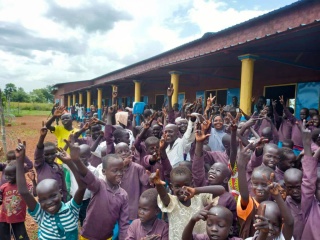 Children standing outside at school, smiling and holding their hands in the air.