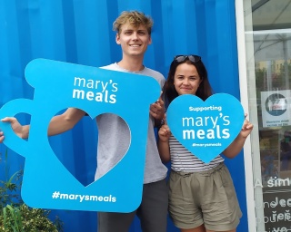 Volunteers holding up Mary's Meals props and smiling into camera. 