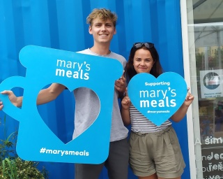 Volunteers holding up Mary's Meals props and smiling into camera.