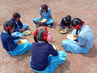 A group of school girls in India sitting in a circle enjoy their meal at school.
