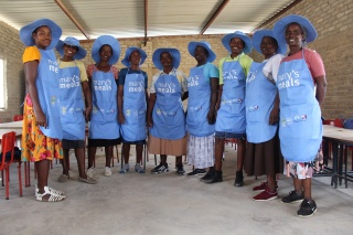 Volunteer cooks standing in a semi-circle in a classroom smiling into camera.