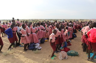 Hundreds of children in school uniforms at school, with the backdrop of a dry and arid desert landscape.