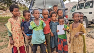 Group of children standing in front of parked vehicles.